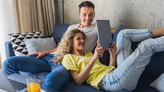 Couple smiling while looking at a tablet together on a couch