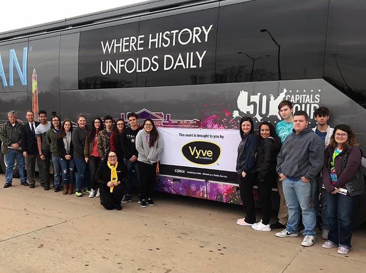 Vyve employees and Shawnee students pose with a Vyve banner outside the CSPAN 50 Capitals Tour bus