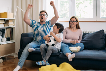 Family sitting on couch cheering as they watch TV